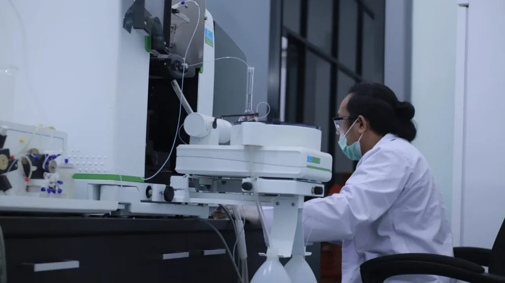 Analis laboratorium berjas putih mengoperasikan instrumen analisis