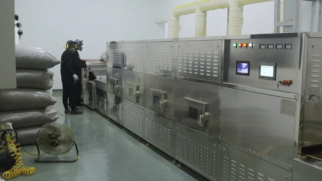 Lini mesin baja tahan karat dengan panel kontrol dan dua pekerja di ujung pengumpanan
